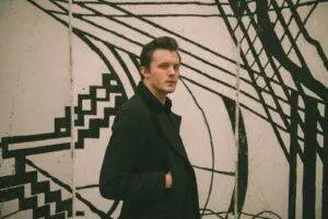 Fashionable male model posing by a unique black and white mural outdoors.