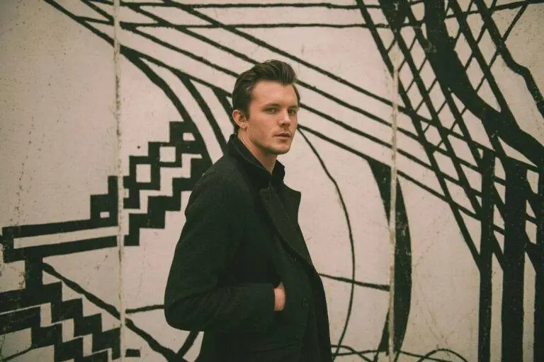 Fashionable male model posing by a unique black and white mural outdoors.