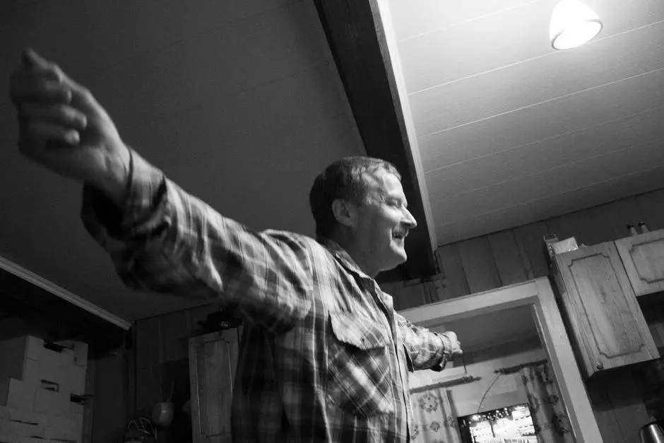 Monochrome image of a smiling man with arms raised inside a cozy setting.