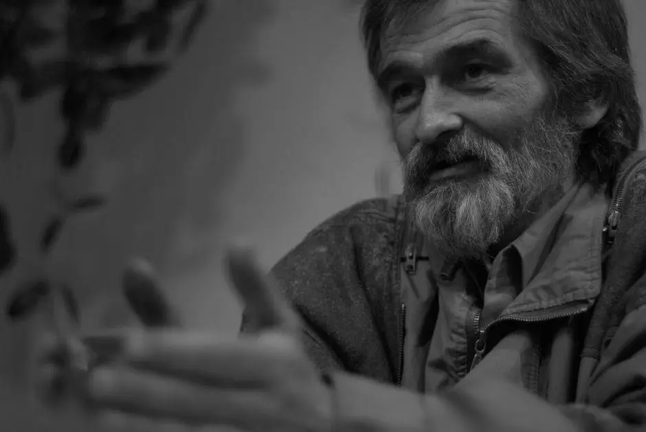 Black and white portrait of an elderly man with a beard and expressive hands, captured in a thoughtful moment.