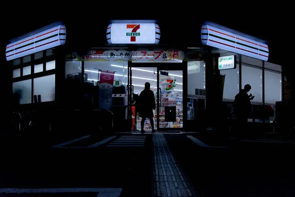 Silhouette of people entering a 7-Eleven store at night in Tokyo's urban setting.