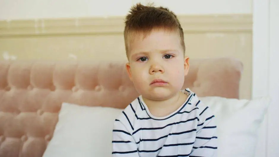 A young child sitting on a couch indoors, displaying a sad expression.