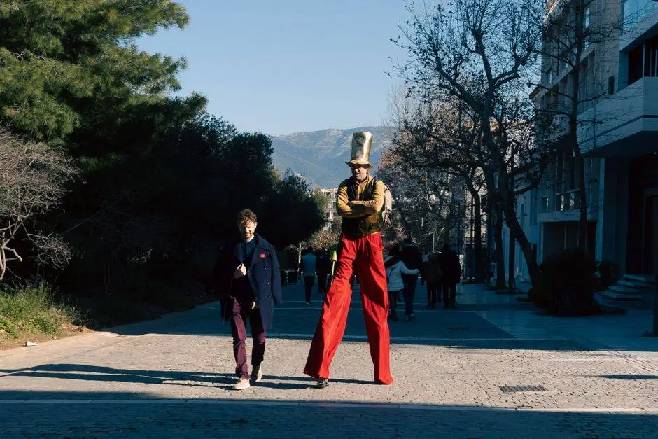 A tall street performer in a colorful costume strolling in Athens on a sunny day.