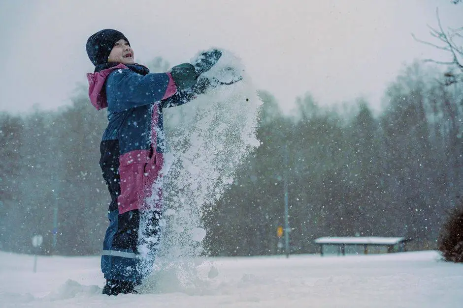 A child in winter clothing joyfully plays with snow outdoors in a snowy landscape.