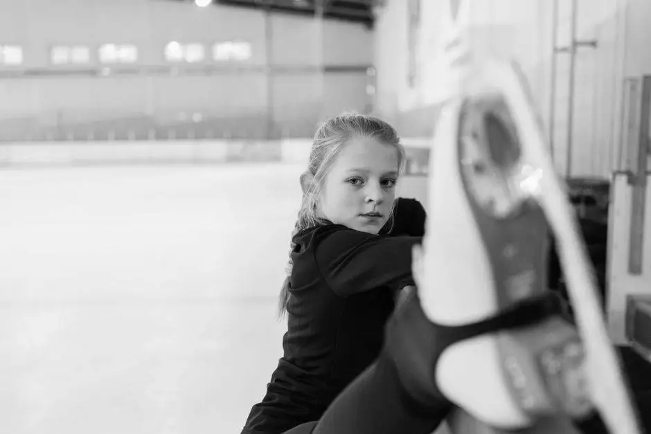 A focused girl practicing figure skating on an indoor ice rink in monochrome.