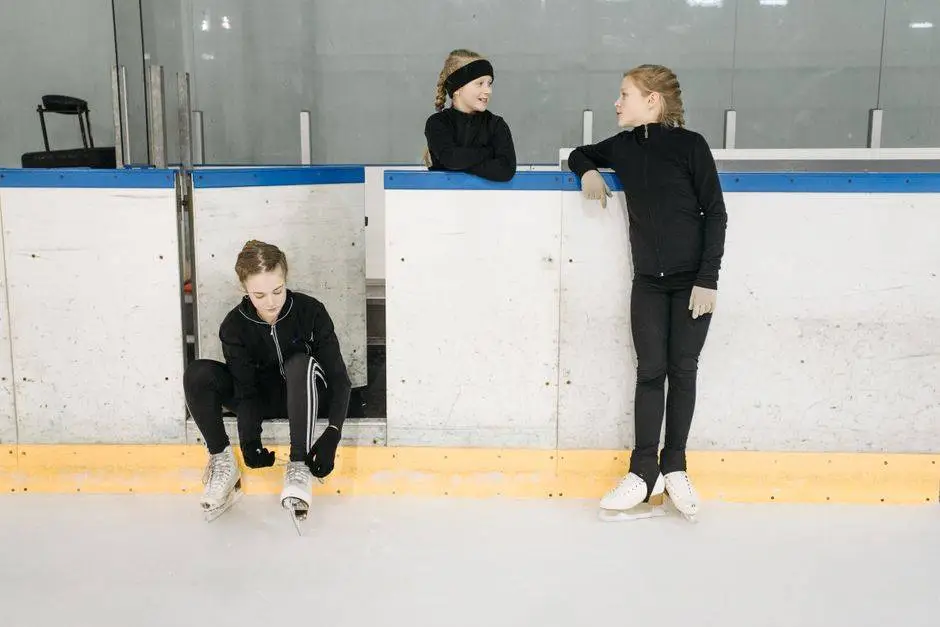 Three young figure skaters preparing for practice at an indoor ice rink.