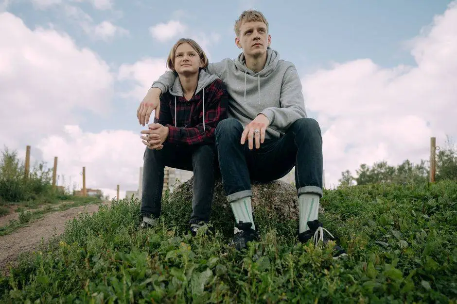 Two young adults sitting together outdoors, enjoying a sunny day with a natural background.
