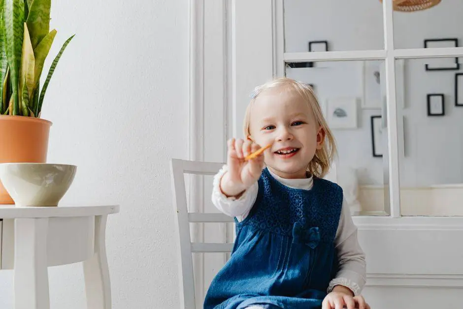 A cheerful young girl smiling while holding out a biscuit indoors.