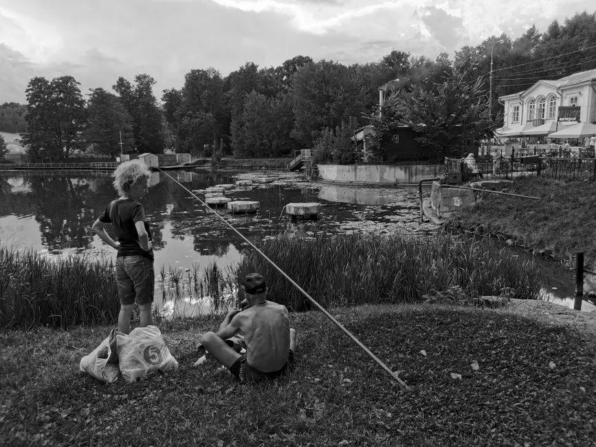 Two people fishing by a serene lake, surrounded by nature. Calm and peaceful atmosphere.
