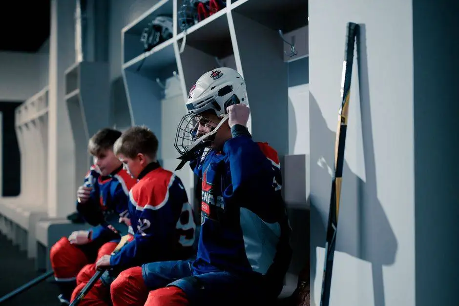Teens in hockey gear getting ready in a dressing room, showcasing teamwork and preparation.