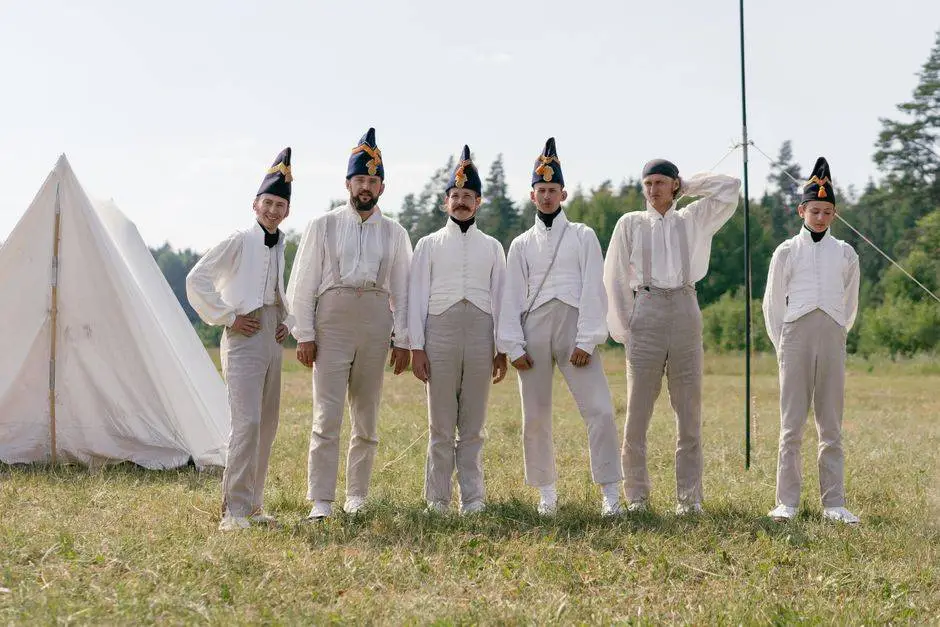 A group of soldiers in historical uniforms standing in a field beside a tent.